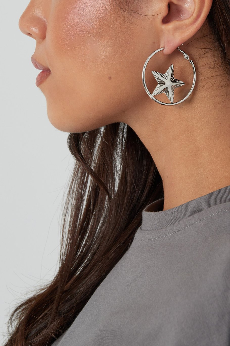 Detalle de pendientes plateados con forma de estrella en aro.

