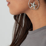 Detalle de pendientes plateados con forma de estrella en aro.

