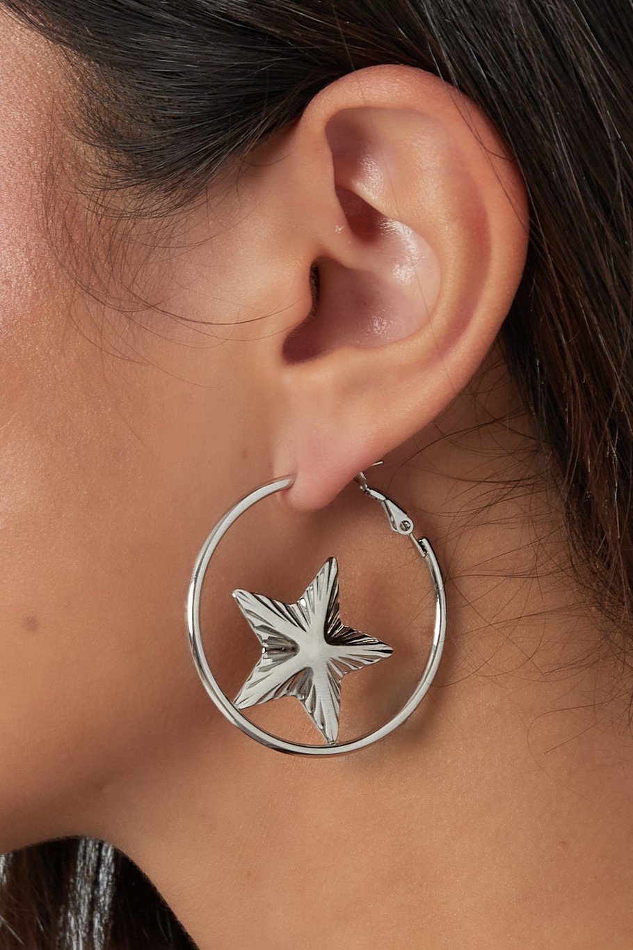Pendientes plateados con estrella central, vista lateral sobre oreja.

