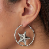Pendientes plateados con estrella central, vista lateral sobre oreja.


