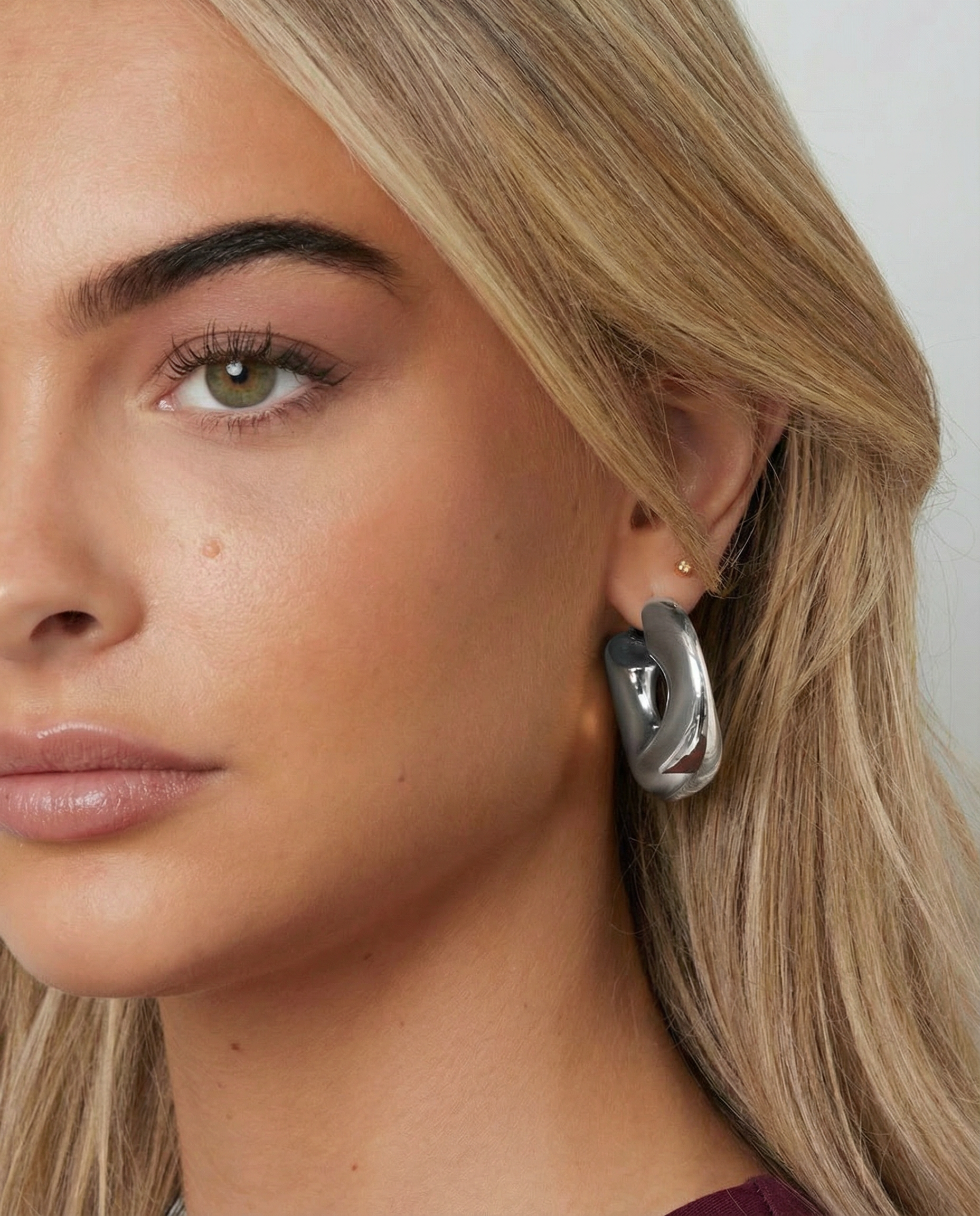 Pendiente plateado de diseño fluido y forma de aro irregular visto en la oreja de una modelo, primer plano lateral.