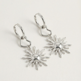 Detalle de pendientes plateados con sol estilizado y aro con corazón.