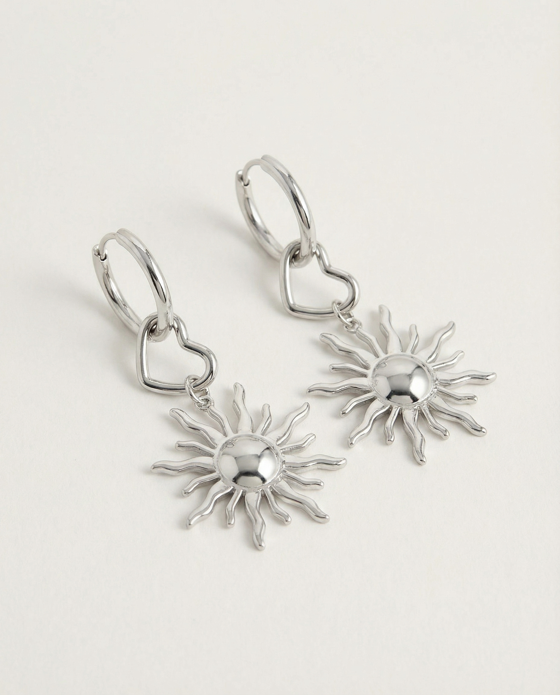 Detalle de pendientes plateados con sol estilizado y aro con corazón.