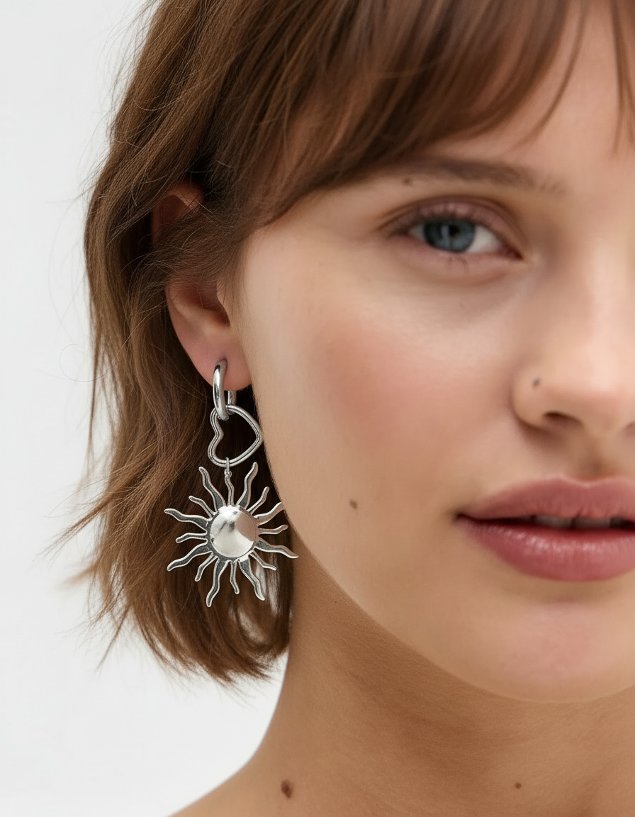 Pendientes plateados con corazón y sol vistos en la oreja de una modelo, estilo moderno.