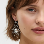 Pendientes plateados con corazón y sol vistos en la oreja de una modelo, estilo moderno.