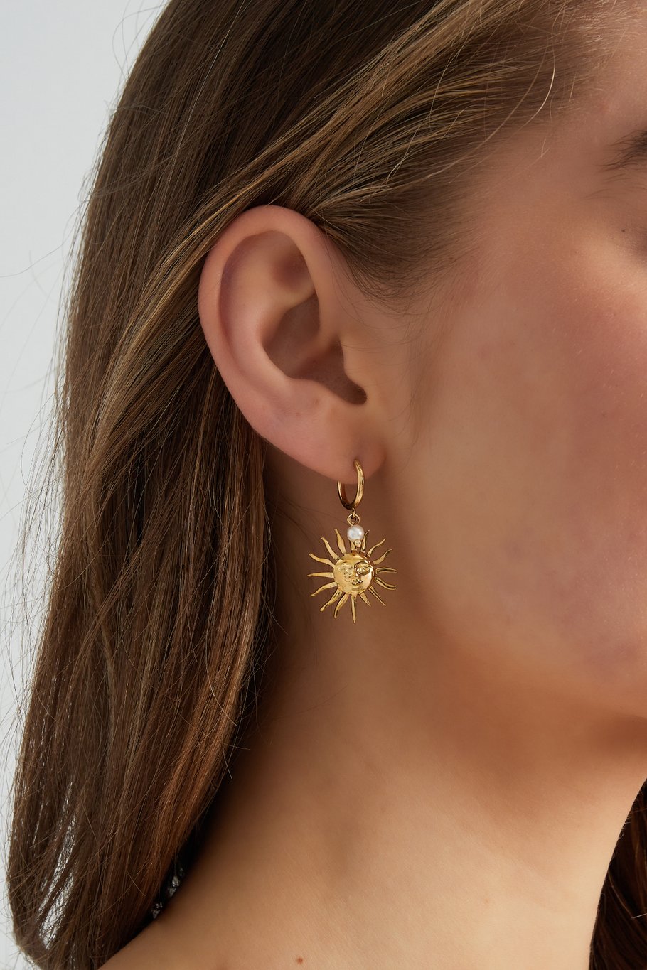 Pendientes plateados con diseño de sol y perla, llevados por modelo de perfil.