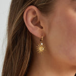 Pendientes plateados con diseño de sol y perla, llevados por modelo de perfil.