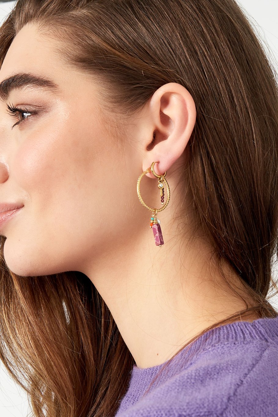Detalle de pendiente dorado con piedra rosa, cuentas de vidrio y perla blanca.