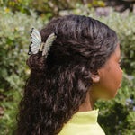 Mujer con cabello largo recogido con pinza mariposa iridiscente Coucou Suzette

