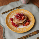 Plato amarillo de cerámica presentado con tortitas y fruta.