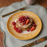 Plato amarillo de cerámica presentado con tortitas y fruta.