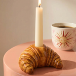 Portavelas de cerámica con forma de croissant y vela blanca sobre una mesa.