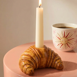 Portavelas de cerámica con forma de croissant y vela blanca sobre una mesa.