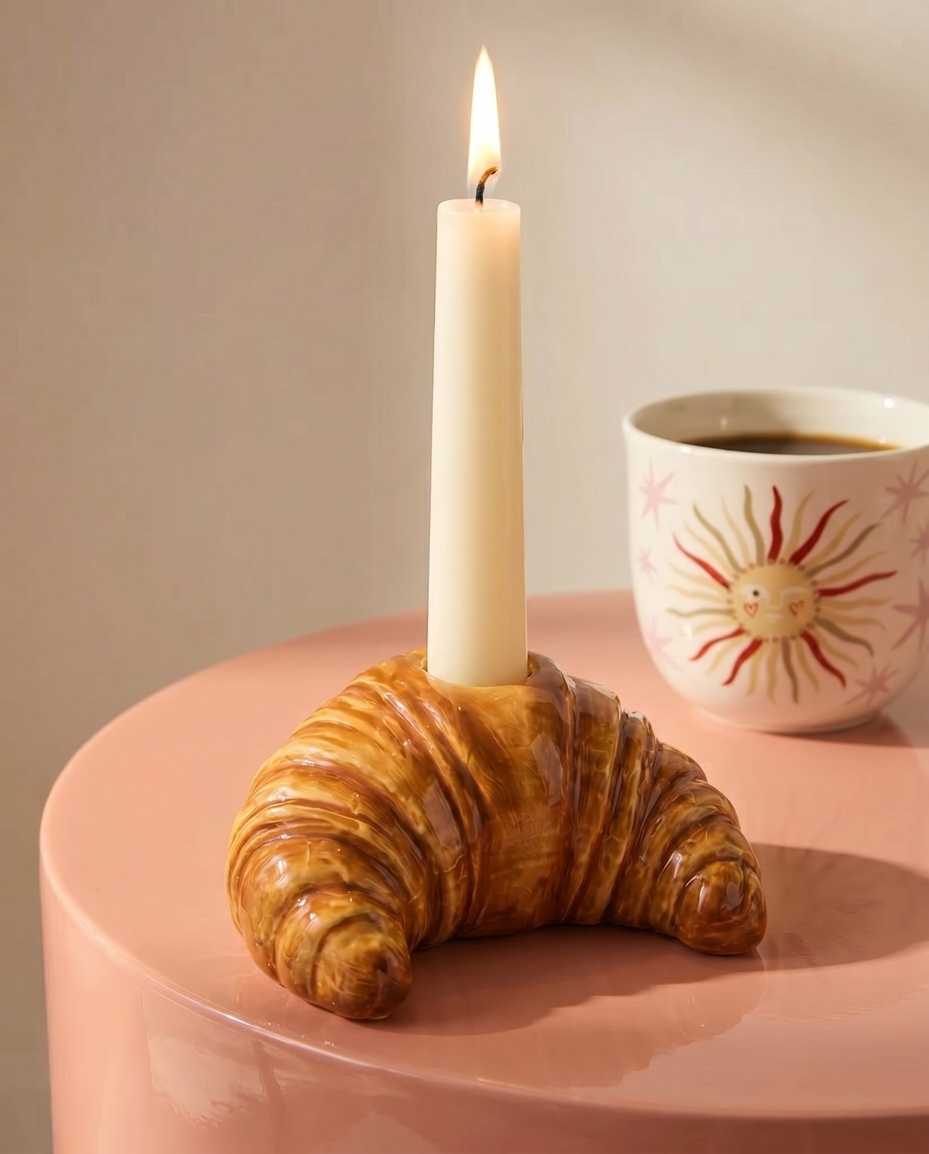 Portavelas de cerámica con forma de croissant y vela blanca sobre una mesa.