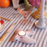 Portavelas en forma de pájaro sobre una mesa decorada con copas vintage. Vela tealight encendida