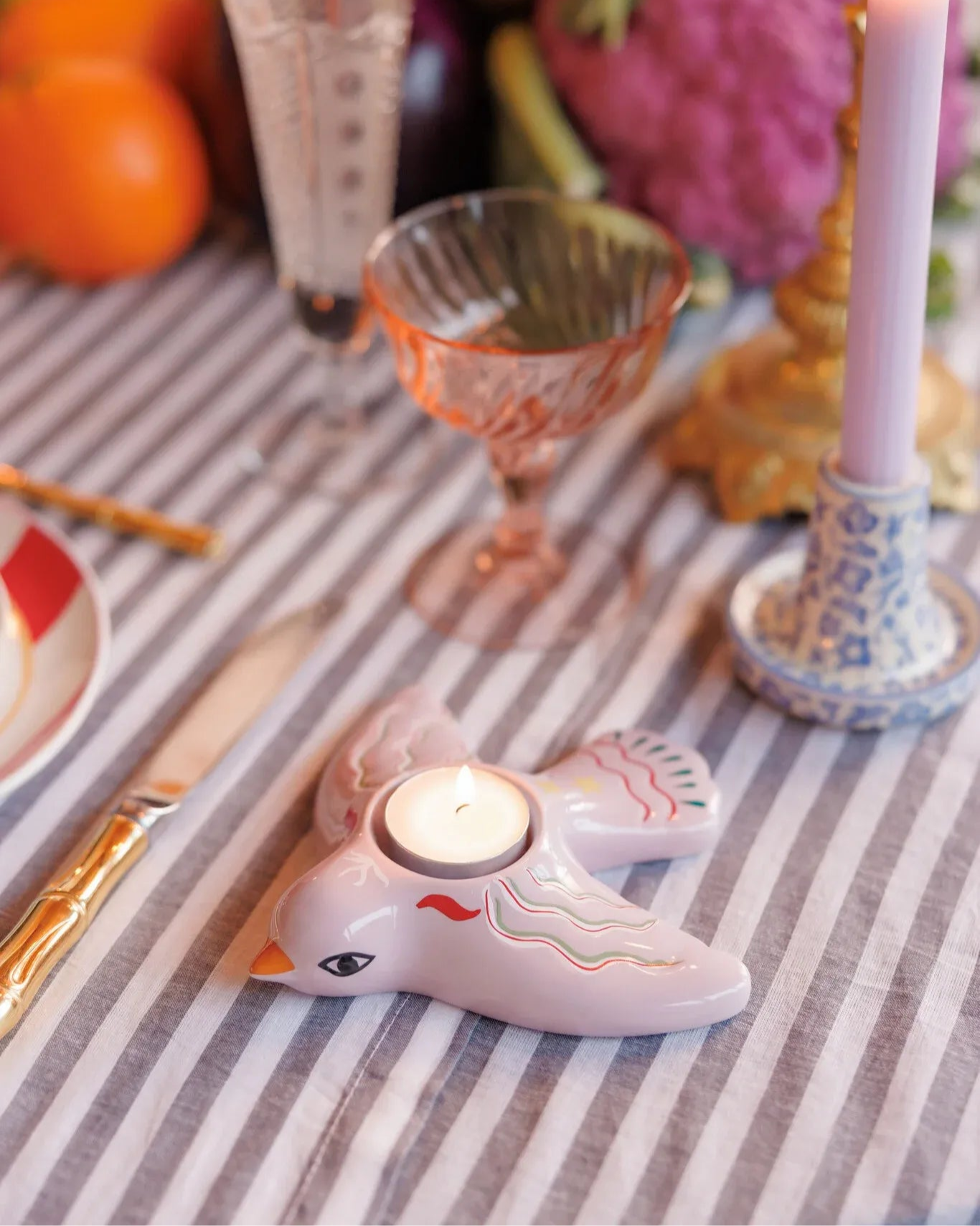 Portavelas en forma de pájaro sobre una mesa decorada con copas vintage. Vela tealight encendida