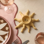 Portavelas de cerámica amarillo con forma de sol sobre una mesa decorada.