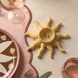 Portavelas de cerámica amarillo con forma de sol sobre una mesa decorada.
