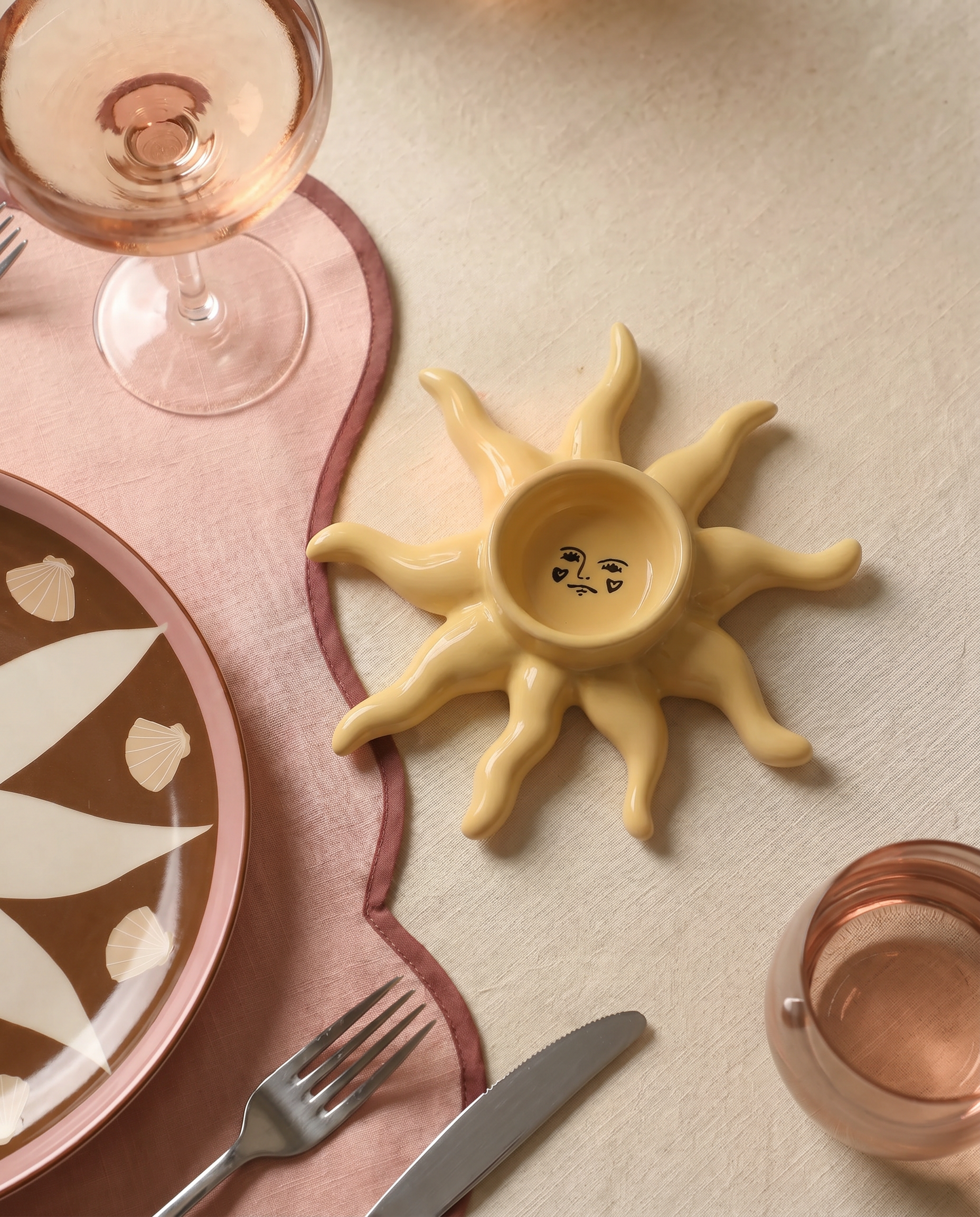 Portavelas de cerámica amarillo con forma de sol sobre una mesa decorada.