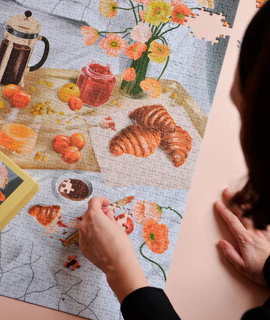 Persona haciendo puzzle artístico de 1000 piezas con temática de brunch