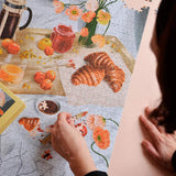 Persona haciendo puzzle artístico de 1000 piezas con temática de brunch