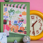 Parte trasera de la caja verde del puzzle Le Lèche-Vitrine de Jour Férié, fotografiada sobre fondo rosa con accesorios decorativos.