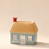 Quemador de incienso PADDYWAX en forma de casa verde con ventanas azules, tejado crema y chimenea roja.