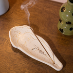Quemador de incienso blanco con diseño de silueta femenina sobre una mesa de madera.