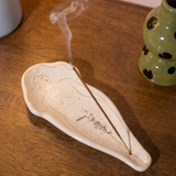 Quemador de incienso blanco con diseño de silueta femenina sobre una mesa de madera.