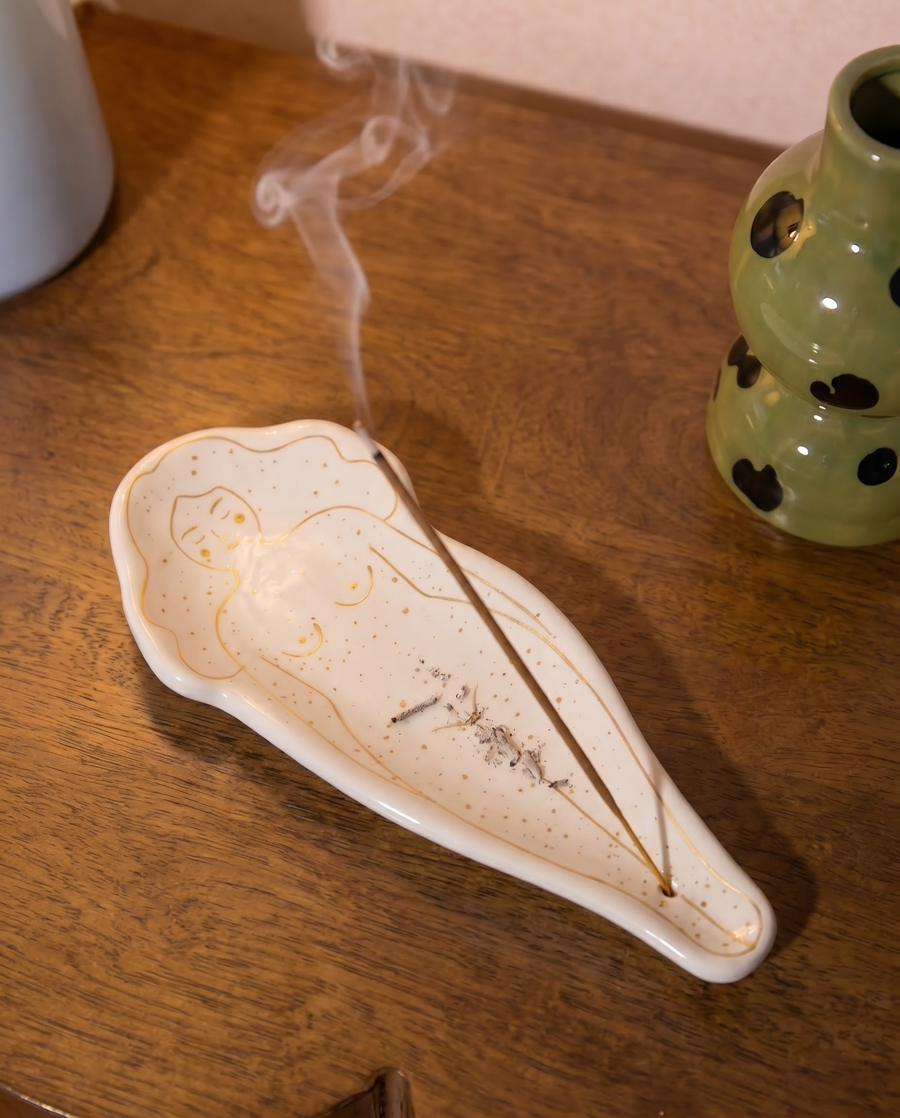 Quemador de incienso blanco con diseño de silueta femenina sobre una mesa de madera.