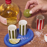 Set de tequila de cerámica con dos vasos verdes sobre bandeja azul, lima y sal, junto a una botella de tequila.