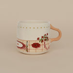 Taza de cerámica con ilustración festiva y asa color beige, vista frontal sobre fondo crema.