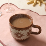 Taza marrón Estrellas y Olas con café caliente.
