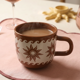 Taza marrón de cerámica con estampado de estrellas y olas sobre mantel rosa.