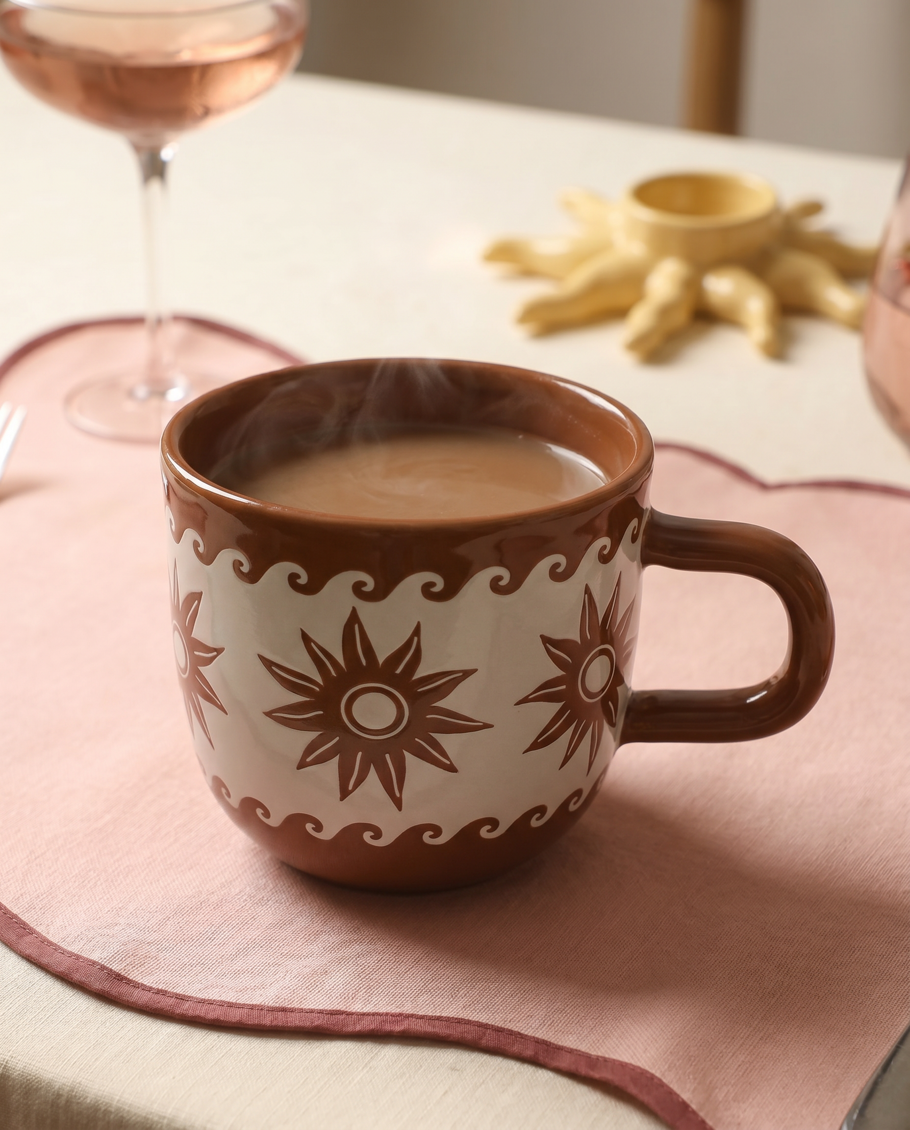 Taza marrón de cerámica con estampado de estrellas y olas sobre mantel rosa.