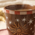 Detalle del estampado de sol y estrellas de la taza de cerámica marrón.