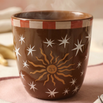 Vista frontal de la taza marrón Sol y Estrellas con café caliente.