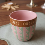 Taza de cerámica rosa con estampado de ondas y borde decorado con lunas.