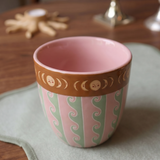 Taza de cerámica rosa con estampado de ondas y borde decorado con lunas.