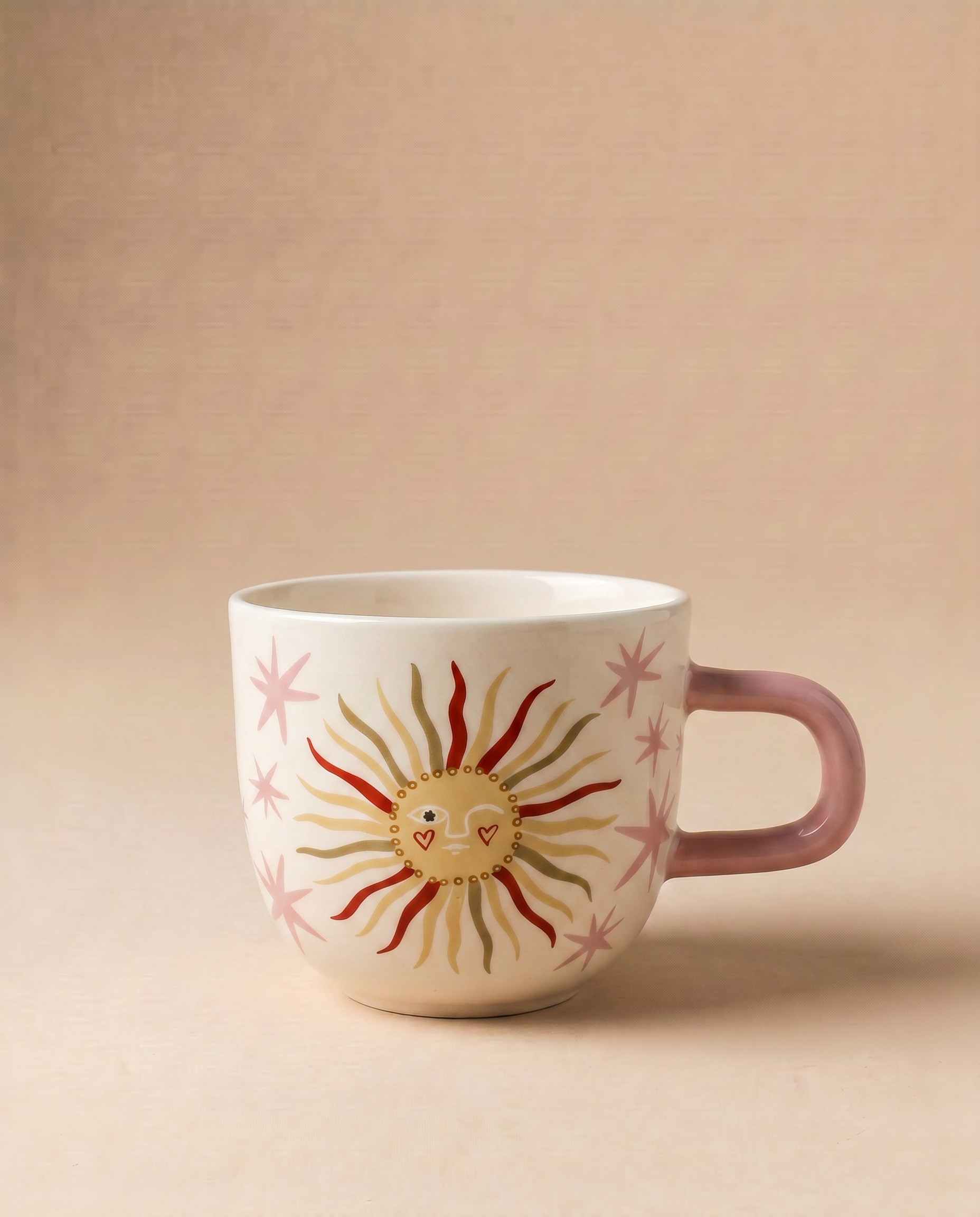 Taza de cerámica rosa con ilustración de un sol sonriente sobre fondo beige.