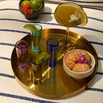 Vasos de chupito de colores con cócteles y frutas sobre bandeja dorada.