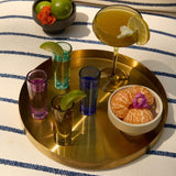 Vasos de chupito de colores con cócteles y frutas sobre bandeja dorada.