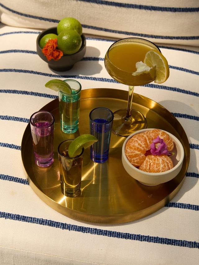 Vasos de chupito de colores con cócteles y frutas sobre bandeja dorada.