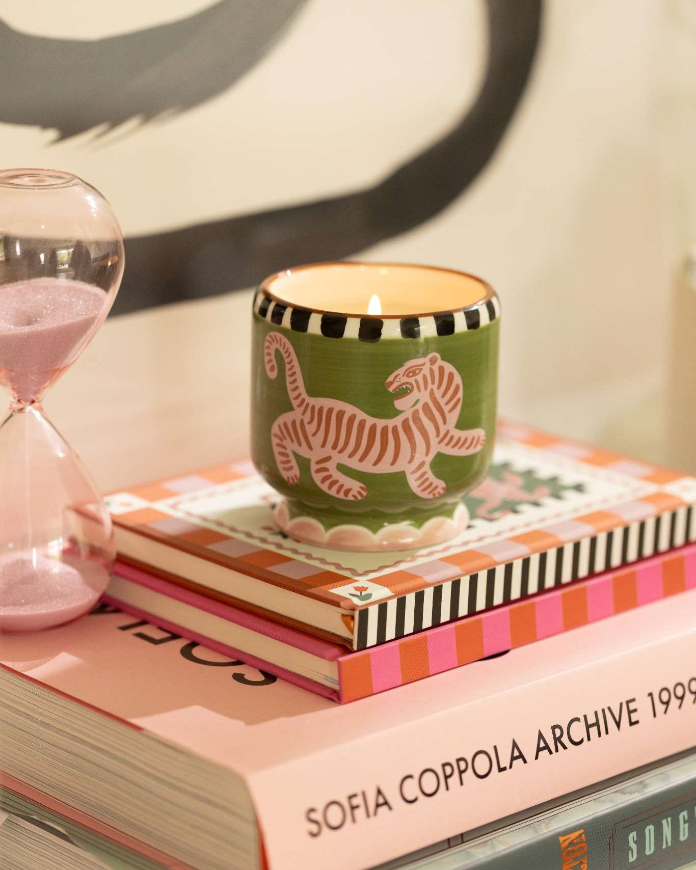 Vela aromática de soja en vaso de cerámica verde con tigre rosa, vista frontal sobre libros