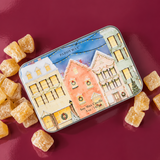 Vela aromática PADDYWAX en lata azul pastel con ilustraciones de casas navideñas.