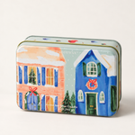 1. Detalle de lata PADDYWAX con casas nevadas, ventanas iluminadas y coronas navideñas.