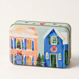 1. Detalle de lata PADDYWAX con casas nevadas, ventanas iluminadas y coronas navideñas.