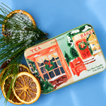 Vela aromática PADDYWAX de naranja y canela en lata metálica con ilustración de tiendas navideñas y buzón rojo.