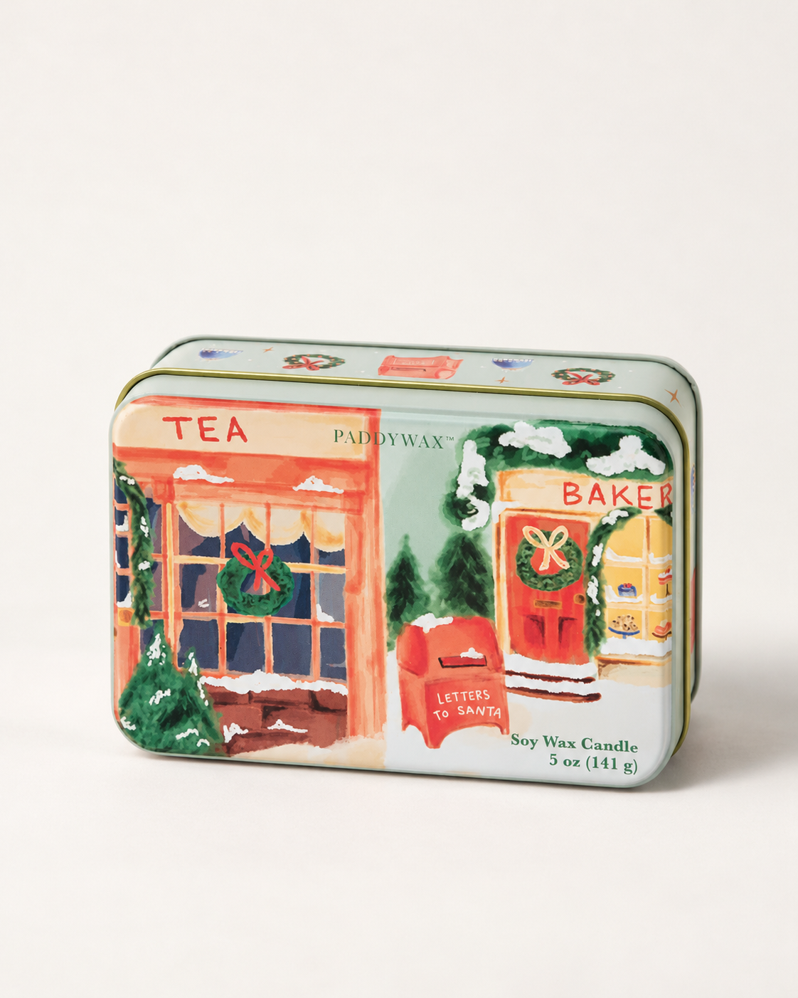 Detalle de lata navideña PADDYWAX con tienda de té, panadería, coronas y buzón de Papá Noel.